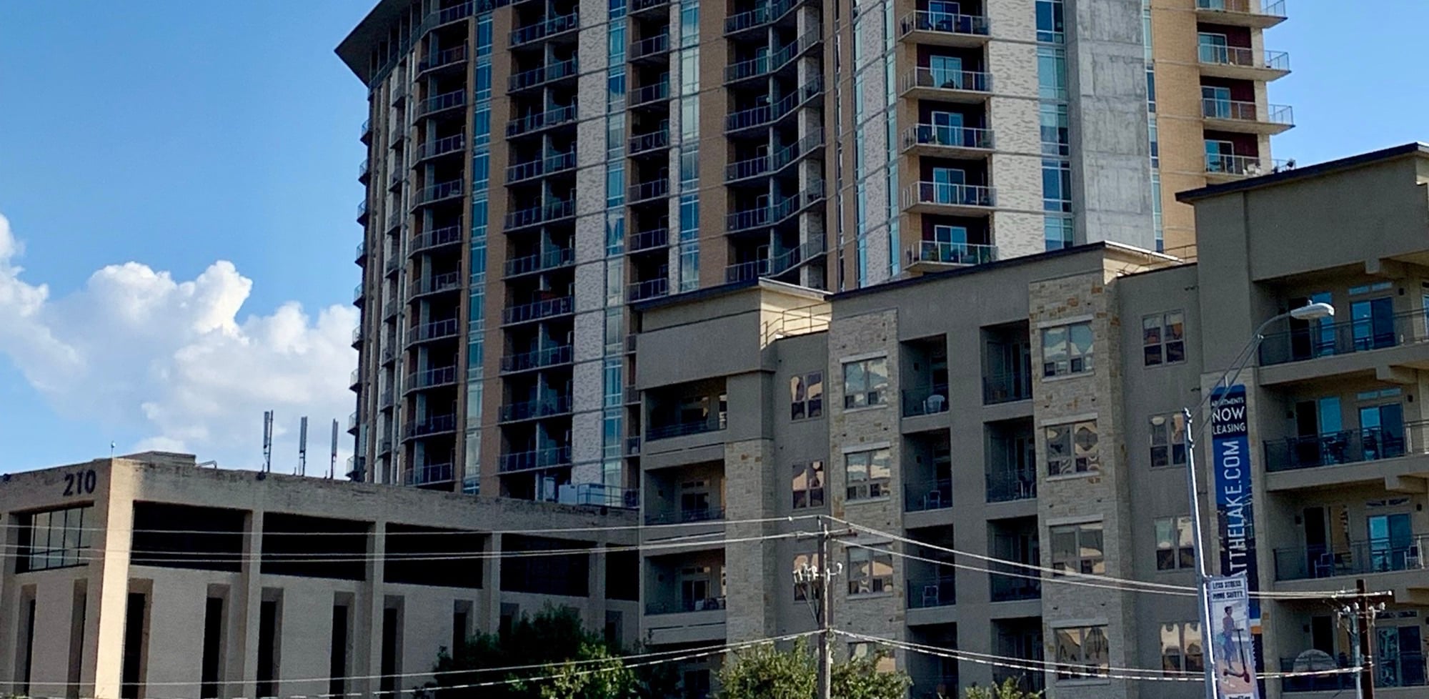 An Austin apartment tower with balconies and a "Now Leasing" banner on a street pole