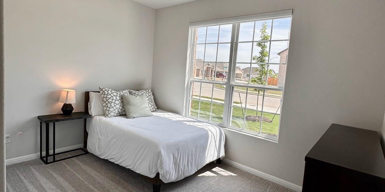 A furnished bedroom at Chapala with a made bed, nightstand, lamp, and a large sunny window