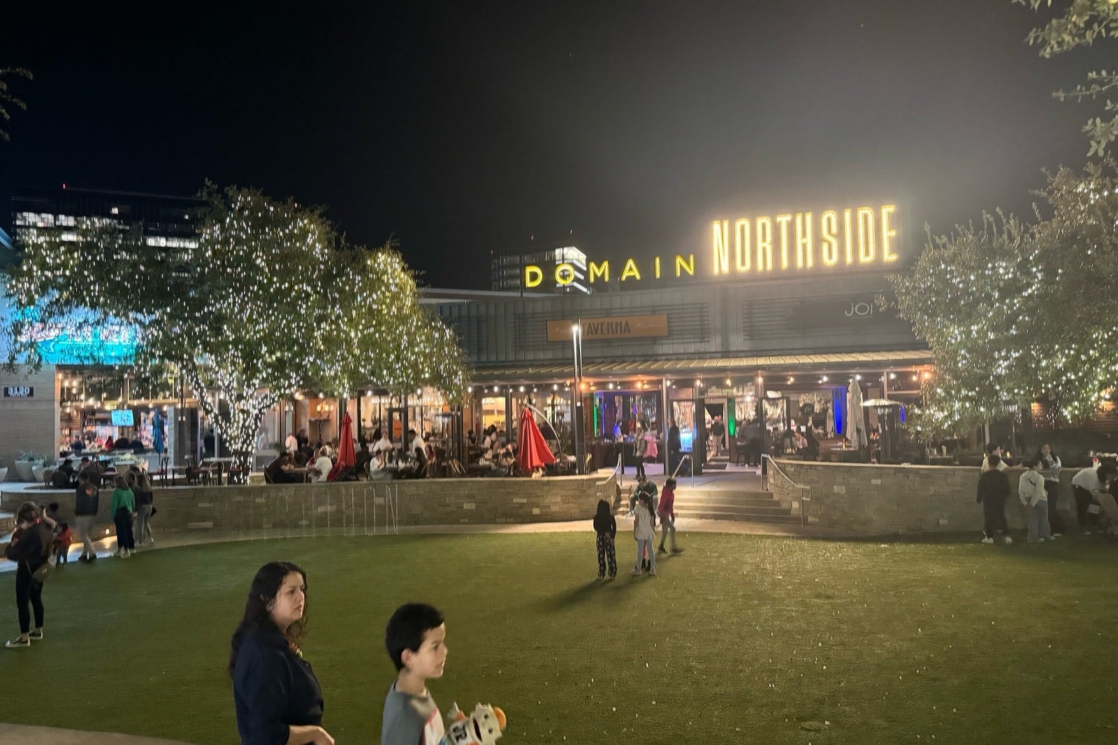 The Domain Northside at night, with string lights over a lawn and a lit Domain Northside sign