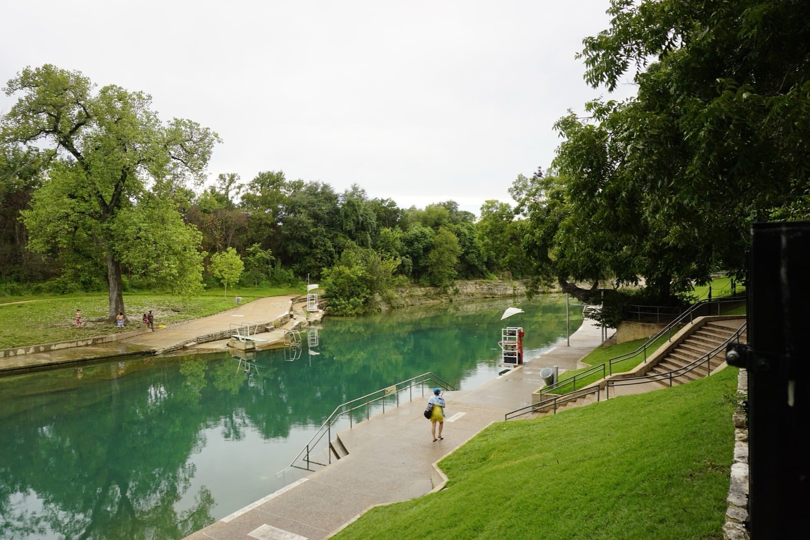 Barton Springs Pool, a spring-fed pool with clear green water surrounded by trees and lawn
